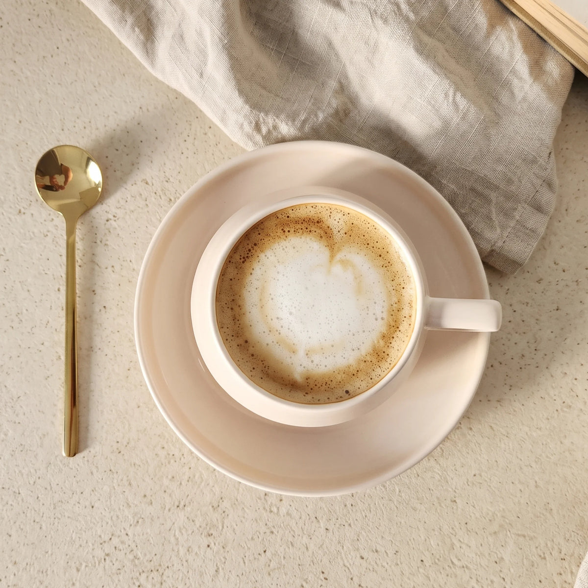Vedere de sus a unei cești bej cu cafea, farfurioară și linguriță aurie